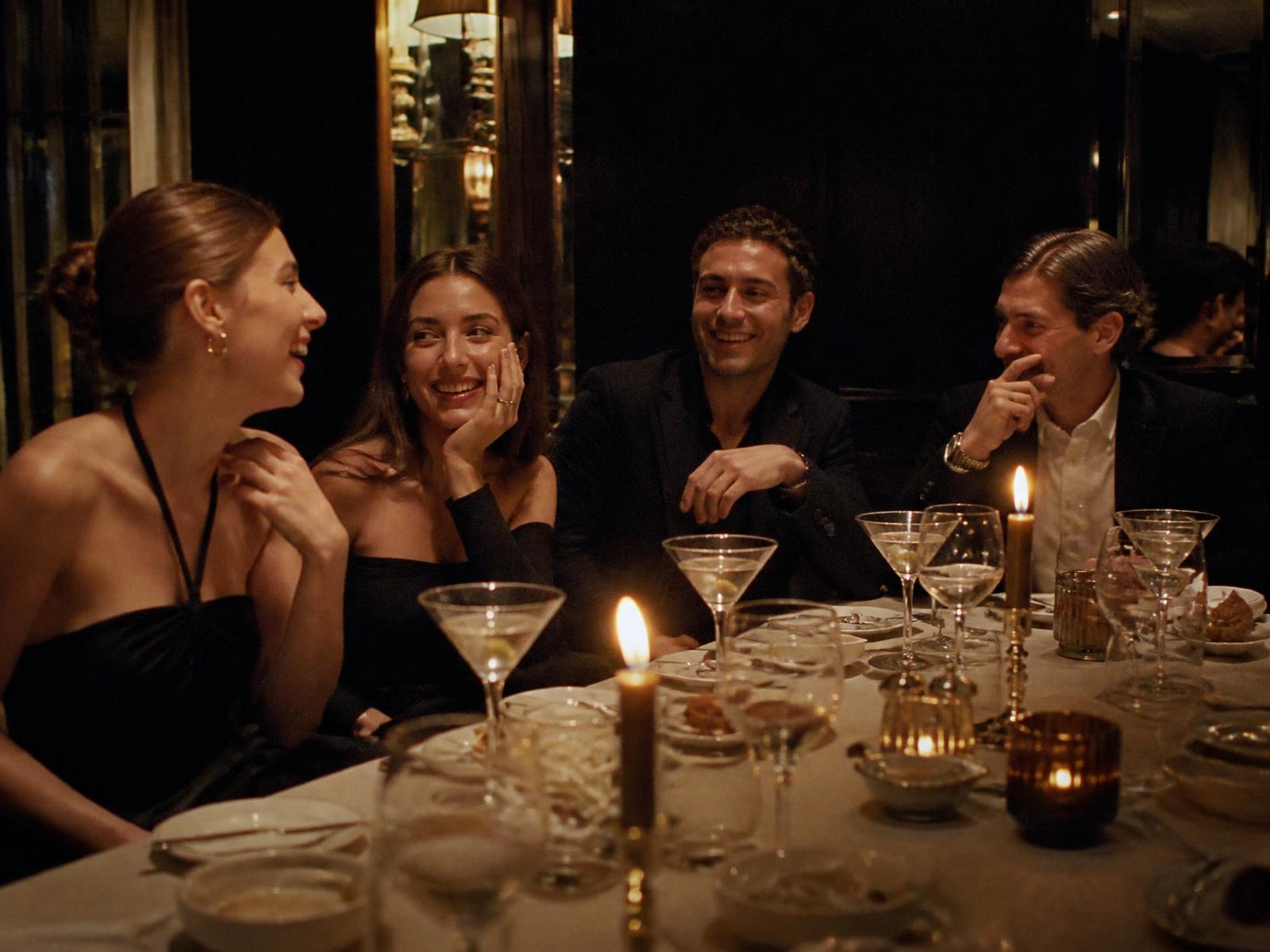 Four friends laughing around a candlelit dinner table in a dim restaurant